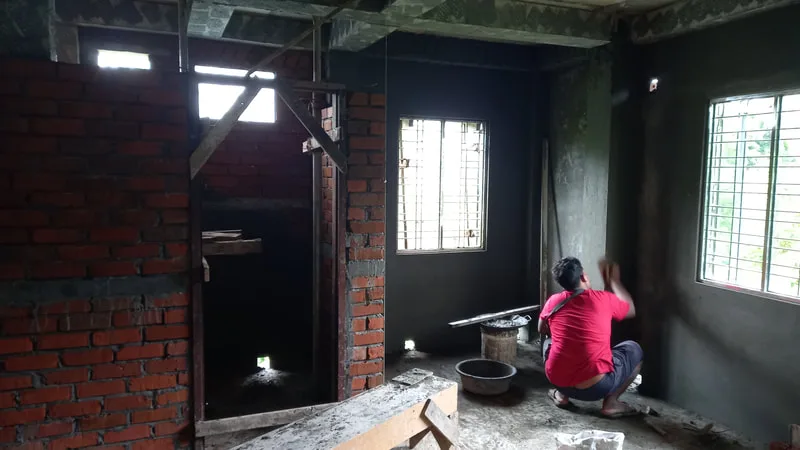 Worker plastering a wall beside a window
