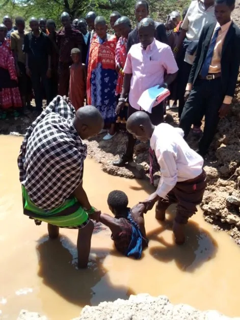 Men assisting at a baptism in a muddy pool