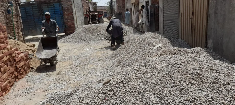 Workers moving gravel in a narrow street