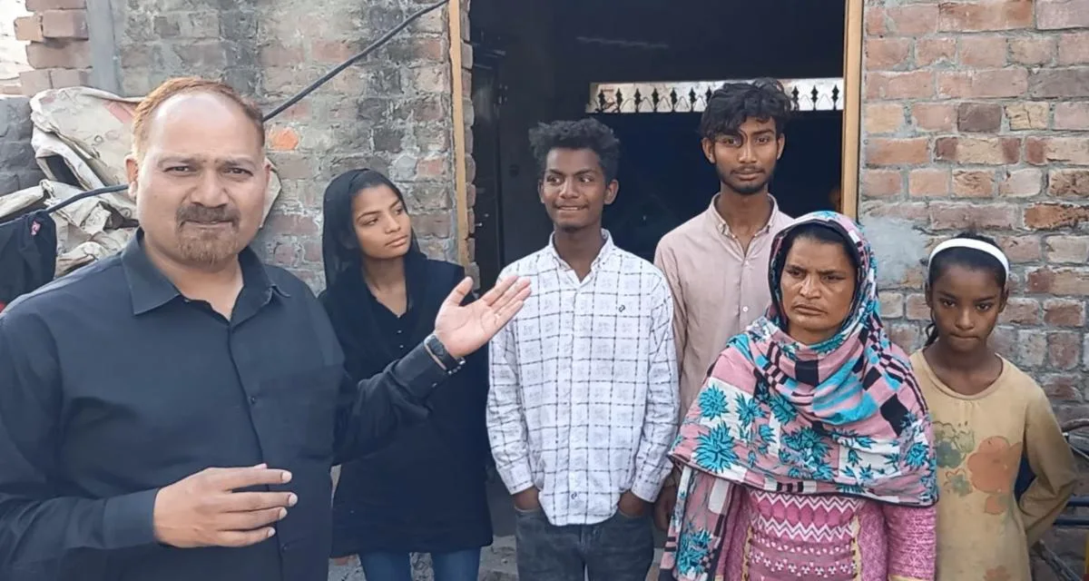 Pastor Shaukat standing with a family outside a brick house