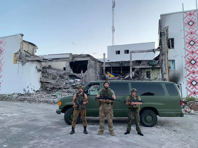 People standing beside a green van and damaged buildings