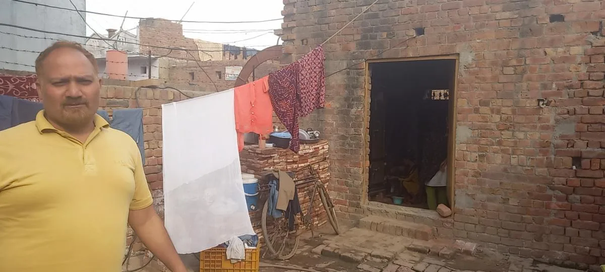 A man standing outside a brick house with laundry hanging nearby