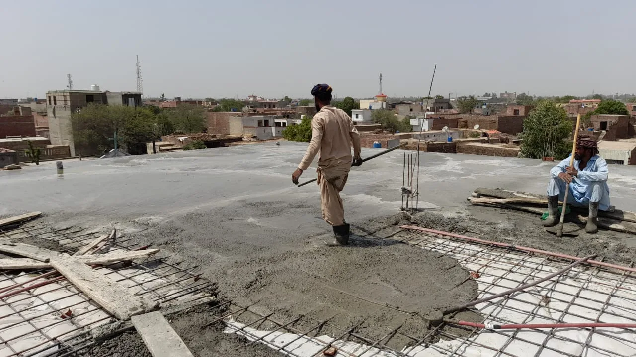 Worker spreading concrete across a roof slab