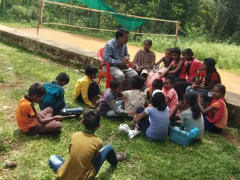 An adult reading with children seated on the grass