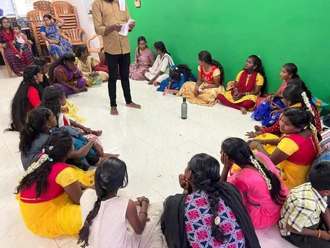 An adult addressing children seated around a room