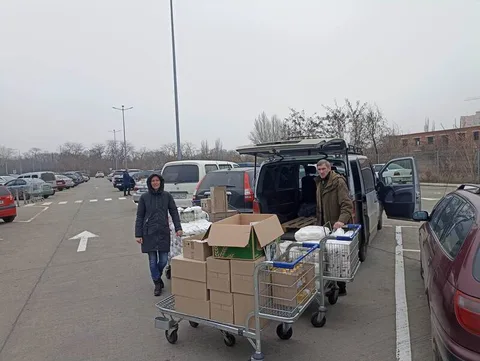 People unloading supplies beside parked vehicles