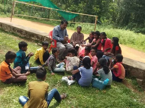An adult holding an open book while children sit on the grass