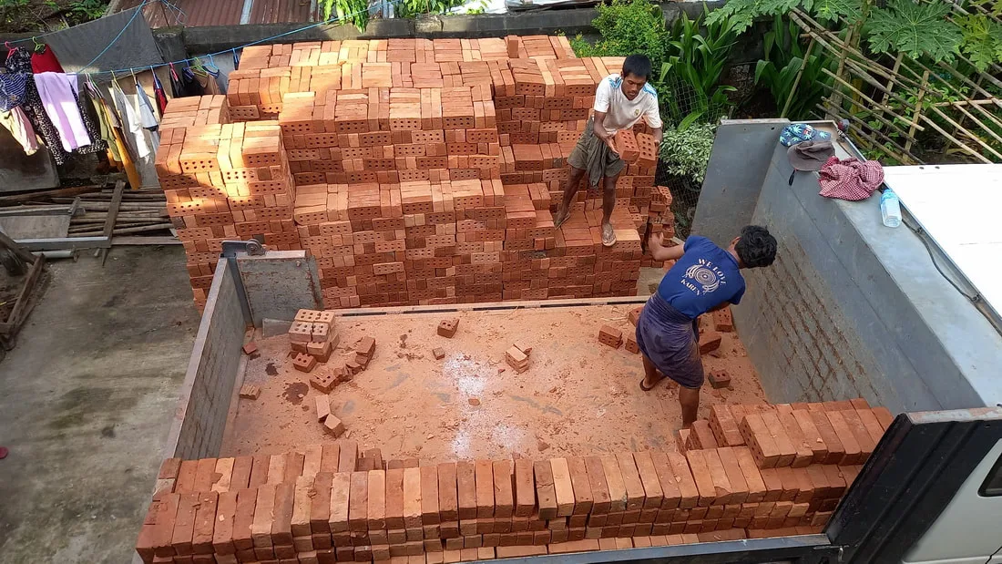 Workers moving bricks beside a construction site