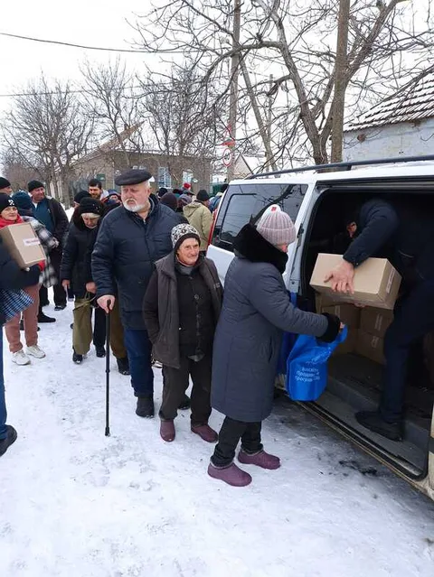 People receiving supplies beside a van in snow