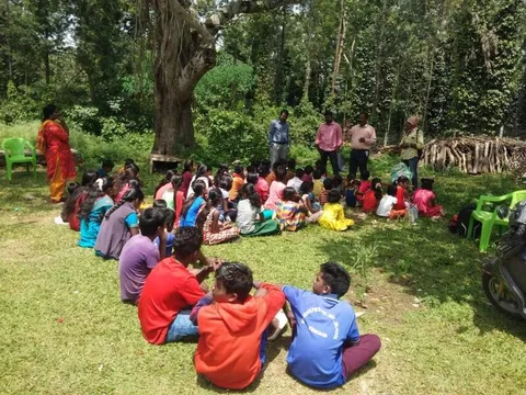 Children and adults gathered on the grass beneath trees
