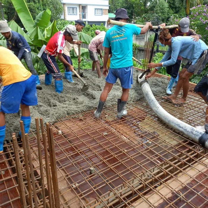 Workers pouring concrete over floor reinforcement