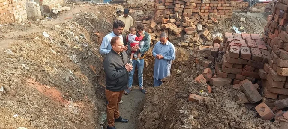 People beside excavated ground and stacks of bricks
