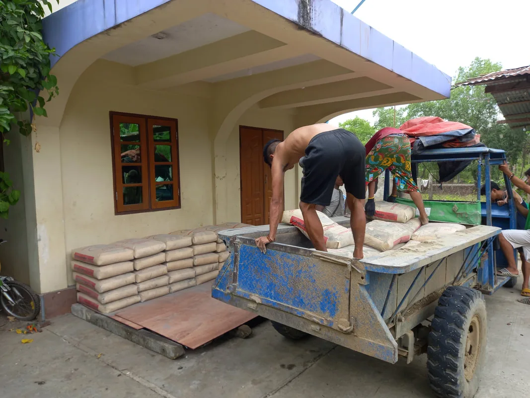 Workers unloading cement bags beside a building