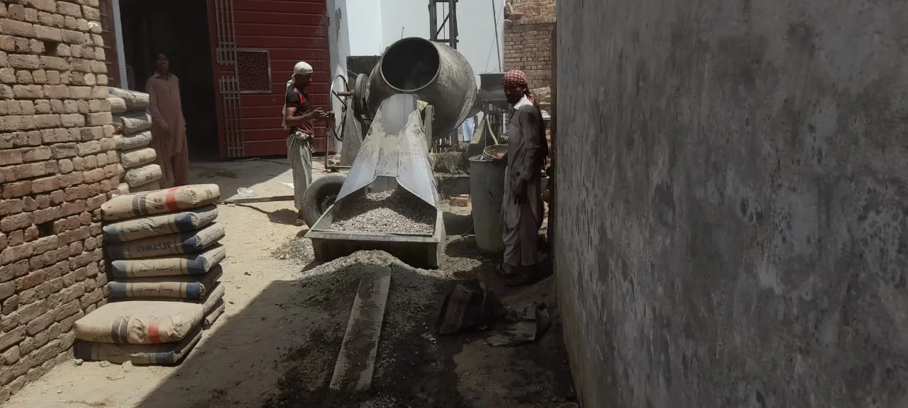 Workers operating a concrete mixer beside cement bags