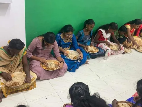 Children eating from plates while seated beside a green wall
