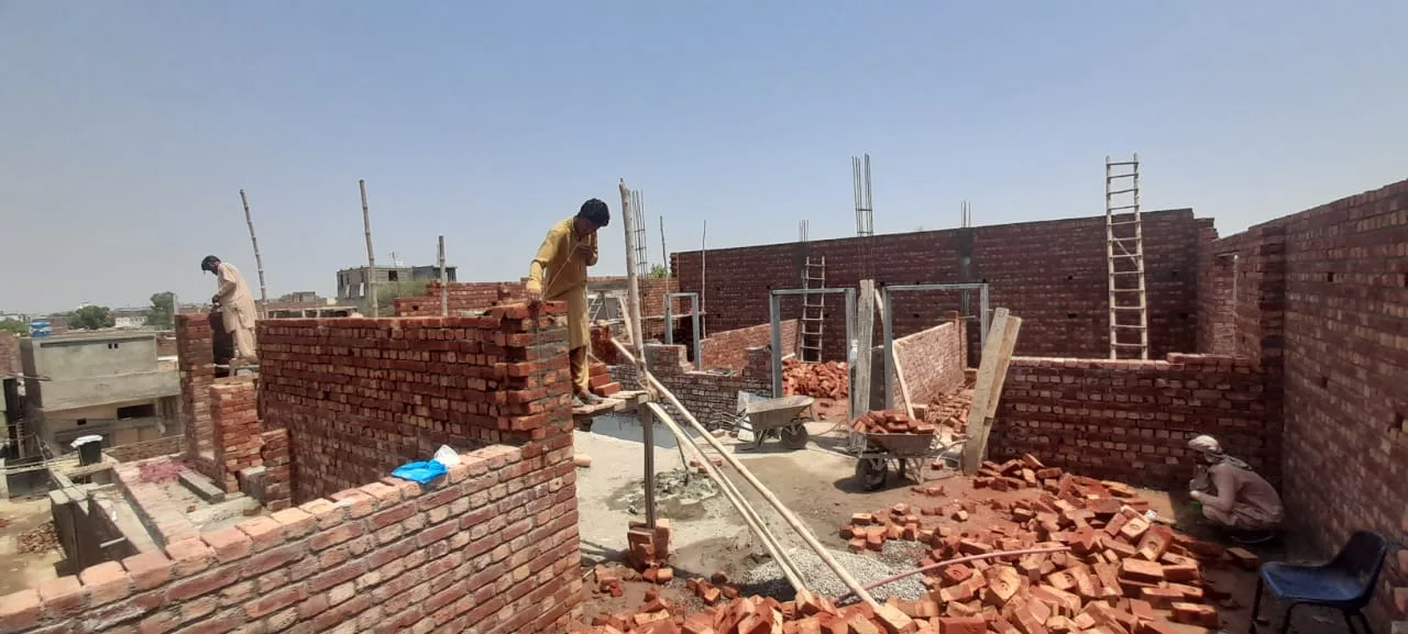 Worker building a brick wall beside a ladder